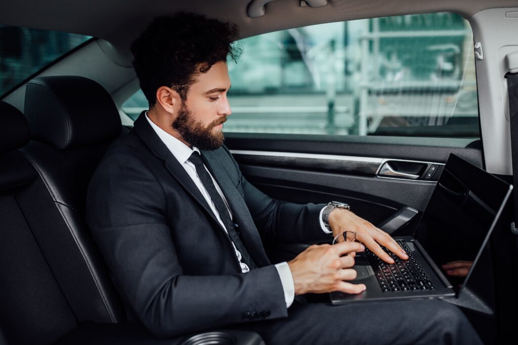 handsome bearded smiling top manager black suit working his laptop backseat car 1